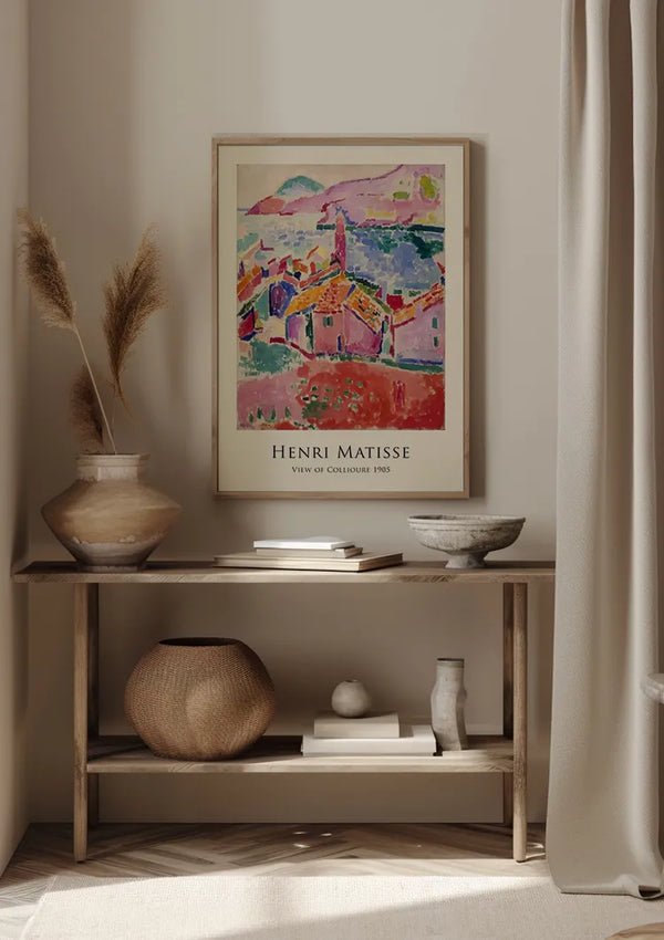 Een ingelijst CollageDepot H. Matisse 1905 schilderij getiteld "Gezicht op Collioure 1905" hangt magnetisch boven een houten tafel. Op de tafel staat een grote vaas met gedroogde planten, een kleine kom, een geweven mand en andere decoratieve voorwerpen. Gordijngordijnen hangen aan de rechterkant.,Lichtbruin