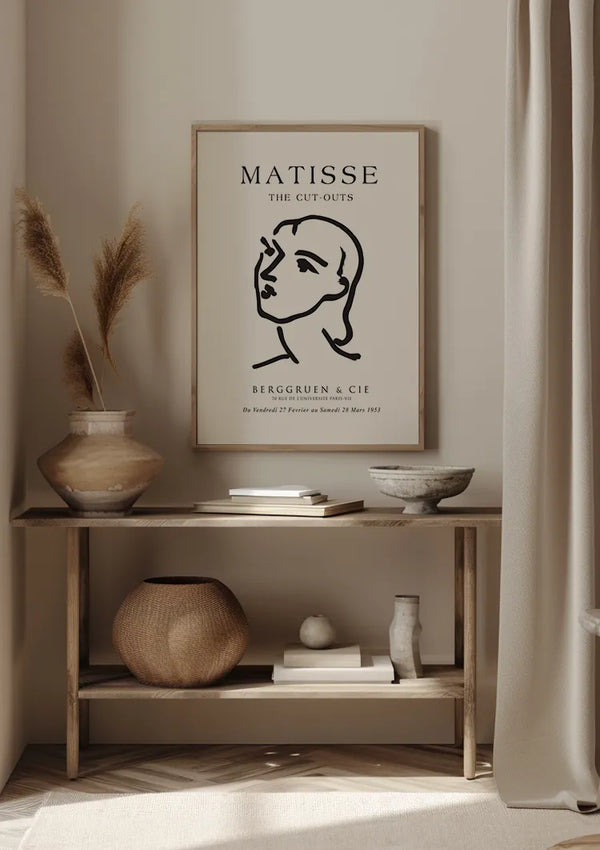 Minimalistische woondecoratie met een ingelijste Matisse-kunstprint, CollageDepot "Matisse: The Cut-Outs Black and White Schilderij", aan de muur met behulp van een magnetisch ophangsysteem. Op een houten consoletafel staan verschillende decorartikelen in neutrale tinten, waaronder vazen, een kom en een rieten mand. Zacht natuurlijk licht verlicht de scène.,Lichtbruin