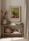 Een ingelijst CollageDepot Claude Monet Bouquet Of Sunflowers Schilderij hangt aan een beige muur boven een houten consoletafel. Op de tafel staan twee vazen, een kom en een geweven mand. In een van de vazen staat pampasgras. Het zonlicht filtert door witte gordijnen en werpt zachte schaduwen op deze elegante wanddecoratie.,Lichtbruin
