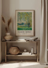 Een minimalistische kamer met neutrale tinten met een ingelijst Claude Monet The Willows Schilderij van CollageDepot als middelpunt van de wanddecoratie. Hieronder staat op een houten plank een decoratieve vaas met gedroogde planten, een geweven mand, een klein beeldhouwwerk en twee gestapelde boeken. Rechts hangt een beige gordijn.,Lichtbruin