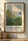 Een ingelijst schilderij van Claude Monet getiteld "Bloemenbedden bij Vétheuil" van de kunstenaar, gedateerd 1881, hangt aan de muur met behulp van een magnetisch ophangsysteem. Het kunstwerk toont kleurrijke bloembedden met groen tegen een sereen landschap. Op een tafel onder het schilderij staat een vaasje met takken. Het gebruikte product is de Claude Monet Flower Beds At Vétheuil Schilderij van CollageDepot.,Lichtbruin