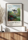 Een ingelijst schilderij van Claude Monet A Corner The Garden With Dahlias van CollageDepot hangt aan een witte muur boven een houten kast, met behulp van een magnetisch ophangsysteem. Links van de kast staat een vaas met pampasgras en rechts een stapel boeken die deze elegante wanddecoratie compleet maken.,Zwart