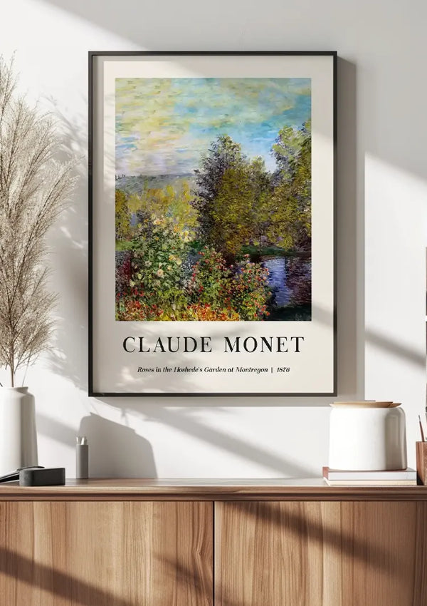 Een ingelijste poster van CollageDepot Claude Monet Roses In The Hoshedé's Garden at Montregan Schilderij hangt aan een witte muur boven een houten kast. In de kast staat een witte vaas met gedroogde planten en een stapel boeken. Zonlicht verlicht de impressionistische kunstscène, versterkt door het magnetische ophangsysteem.,Zwart