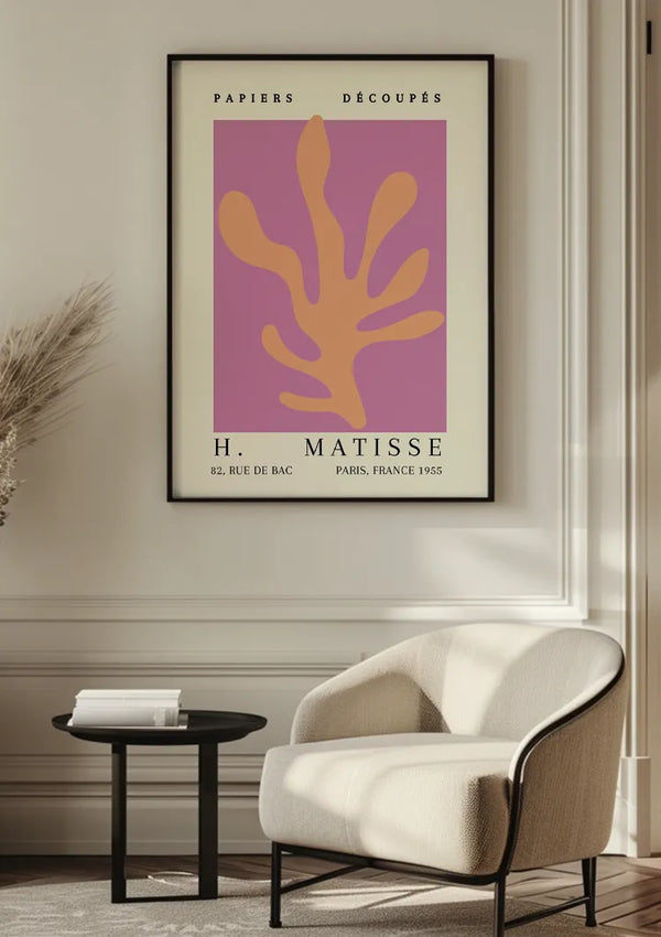 Een minimalistische kamer is voorzien van een ingelijste CollageDepot H. Matisse 1955 Schilderij aan de muur. Het kunstwerk toont een abstracte oranje vorm op een paarse achtergrond. Onder de print bevindt zich een lichtbeige fauteuil en een klein rond zwart bijzettafeltje. De lichtgekleurde muur en vloer vullen de levendige wanddecoratie perfect aan.,Zwart