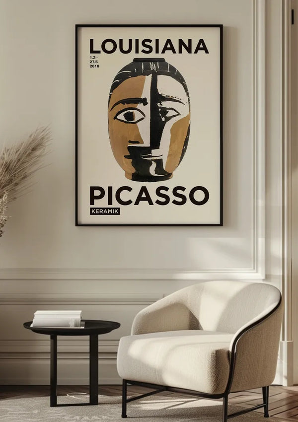 Aan een lichtgekleurde muur hangt een ingelijste poster met een gestileerd gezicht met de tekst "Picasso - Louisiana Schilderij" van CollageDepot, beveiligd door een magnetisch ophangsysteem. Hieronder staat een moderne fauteuil en een klein zwart bijzettafeltje met een boek. Zonlicht filtert door een nabijgelegen, onzichtbaar raam.,Zwart