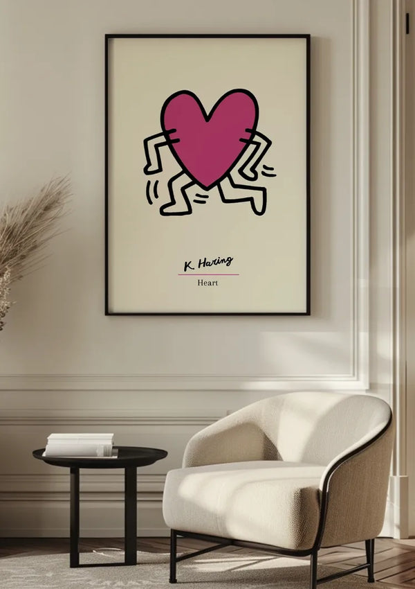A K. Haring - Hartschilderij van CollageDepot met een roze hart met armen en benen, opgehangen aan een witte muur. Onder het hart staat de tekst "K. Haring" en "Hart". Vooraan staat een moderne witte fauteuil en een rond zwart bijzettafeltje met een boek erop. Het schilderij maakt gebruik van een magnetisch ophangsysteem voor eenvoudige weergave.,Zwart