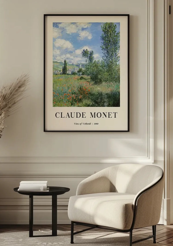 Een ingelijst schilderij van Claude Monet met de titel "Gezicht op Vétheuil | 1880" hangt aan een witte muur boven een moderne beige fauteuil met een zwart bijzettafeltje. Het CollageDepot Claude Monet Landelijk Tafereel Schilderij, met een schilderachtig landschap met bomen en een blauwe lucht, dient als een voortreffelijk stukje wanddecoratie.,Zwart
