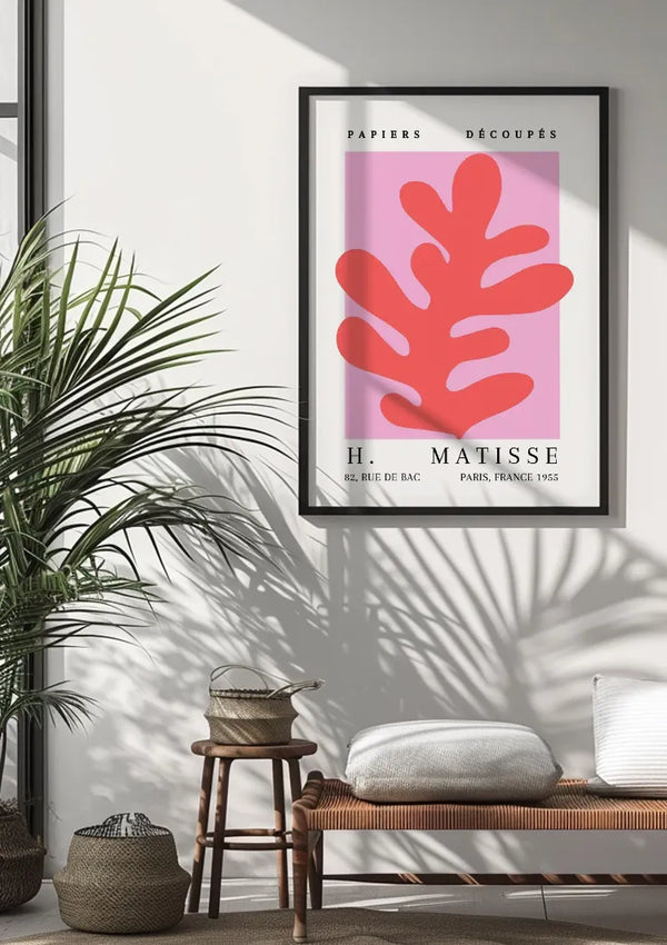 Boven de houten bank hangt een ingelijst H. Matisse - Abstract Bladvorm Schilderij van CollageDepot met abstracte rode vormen op een roze achtergrond. De kamer is voorzien van een grote potplant, geweven manden en kussens, waardoor een moderne en gezellige sfeer ontstaat. In de wanddecoratie is een abstracte bladvorm verwerkt, waarbij schaduwen op de muur worden geworpen.,Zwart