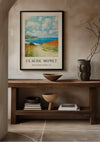 Een ingelijst CollageDepot Claude Monet Path in The Wheat At Pourville Schilderij hangt aan een beige muur boven een houten consoletafel. De tafel is voorzien van een decoratieve kom, een houten vat, een donkere vaas en verschillende gestapelde boeken. Beige tegels met zichtbare voegen bedekken de vloer.,Zwart