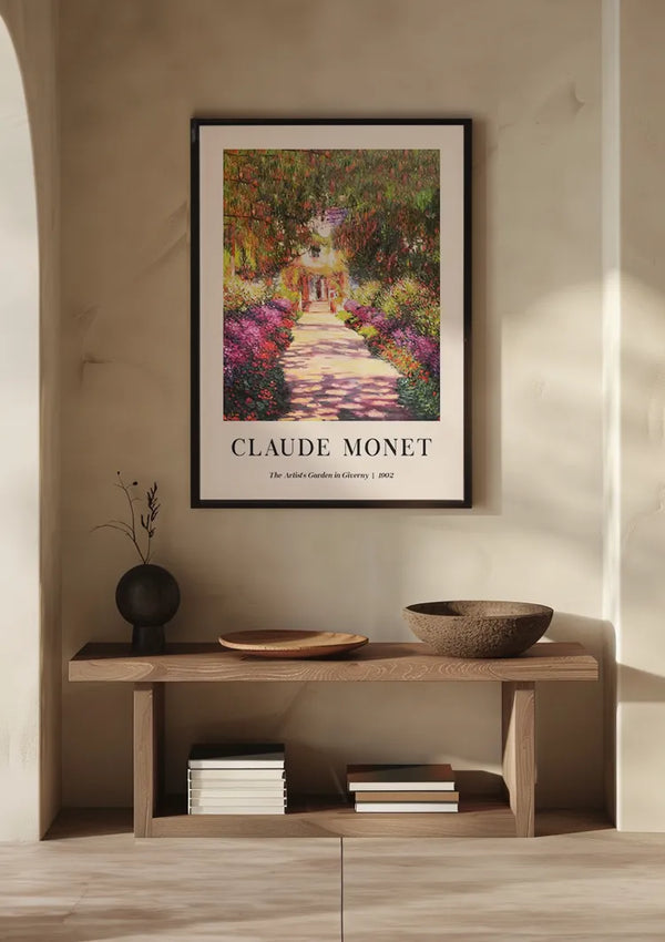 Een ingelijst CollageDepot Claude Monet The Artist's Garden in Giverny 1902 Schilderij hangt als wanddecoratie aan een beige muur boven een houten consoletafel. Op de tafel staat een vaas met een takje, een schaaltje, een brede schaal en verschillende gestapelde boeken.,Zwart