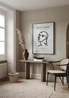 Een minimalistische woonruimte wordt getoond met een houten consoletafel tegen een beige muur. Op de tafel staat een bruine vaas met gedroogd pampagras, een zwarte kom en boeken. Het ingelijste schilderij "Matisse: The Cut-Outs Black and White Schilderij" van CollageDepot hangt aan de muur met behulp van een innovatief magnetisch ophangsysteem. Vlakbij staat een stoel en een geweven mand.,Zwart