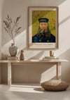 Een ingelijst CollageDepot V. Van Gogh Postbode Portret Schilderij met het schilderij "Portret van Joseph Roulin: 1889", waarop hij wordt afgebeeld in zijn postbode-uniform, hangt aan een lichtgekleurde muur boven een houten consoletafel versierd met verschillende keramische vazen, boeken, en een geweven kussen op de vloer.,Lichtbruin