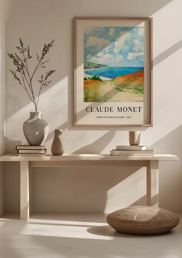 Een minimalistische kamer met een houten bank met twee keramische vazen en een fotolijstje erop. Het ingelijste kunstwerk is een CollageDepot Claude Monet Path in The Wheat At Pourville Schilderij. Voor de bank ligt een geweven kussen op de grond, wat bijdraagt aan de serene sfeer.,Lichtbruin