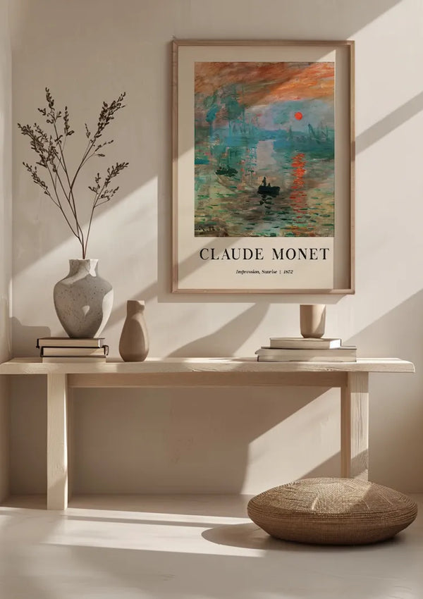 Een minimalistische kamer met daarboven een lichthouten bank met daarboven een CollageDepot Claude Monet Impression, Sunrise Schilderij, gebruikmakend van een magnetisch ophangsysteem. Op de bank staan twee vazen en een stapel boeken. Voor de bank ligt een rond geweven kussen op de grond. De zonsopgang werpt zachte schaduwen over het tafereel.,Lichtbruin