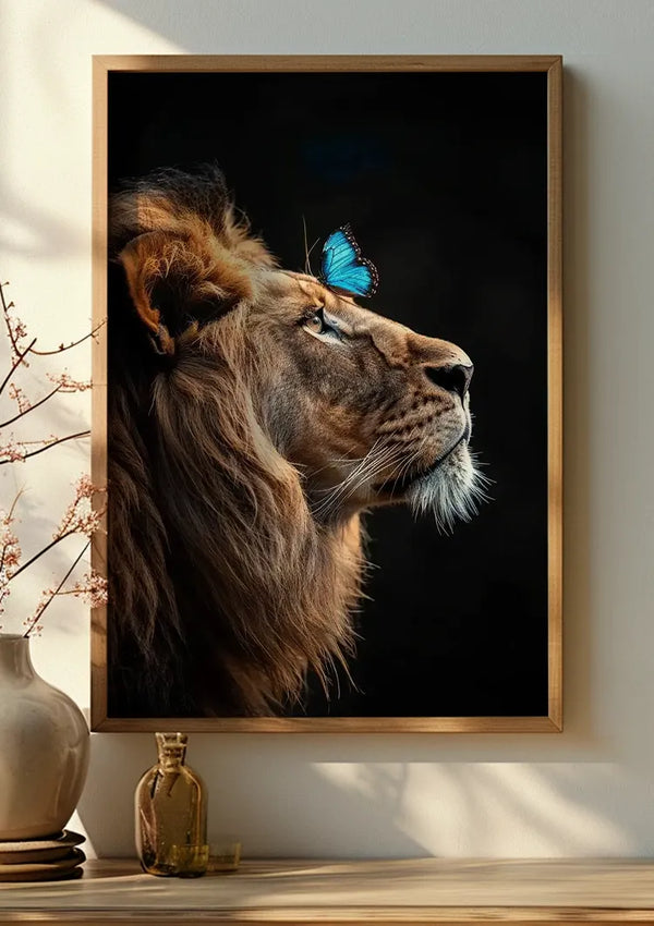 Een ingelijste foto van een leeuw met een blauwe vlinder op zijn neus, The King Schilderij van CollageDepot, siert de muur als prachtige wanddecoratie. Onder het frame bevindt zich een keramische vaas met een tak delicate bloemen, allemaal verlicht door natuurlijk licht vanaf de linkerkant.,Lichtbruin