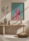 Het minimalistische interieur bestaat uit een houten tafel met een rond kussen op de vloer ervoor. Op tafel staan vazen en boeken netjes gerangschikt. Een ingelijst CollageDepot Vrijheidsbeeld met pluizig roze hoodie-schilderij hierboven toont een persoon in een roze bontjas en kroon die lijkt op het Vrijheidsbeeld.,Lichtbruin