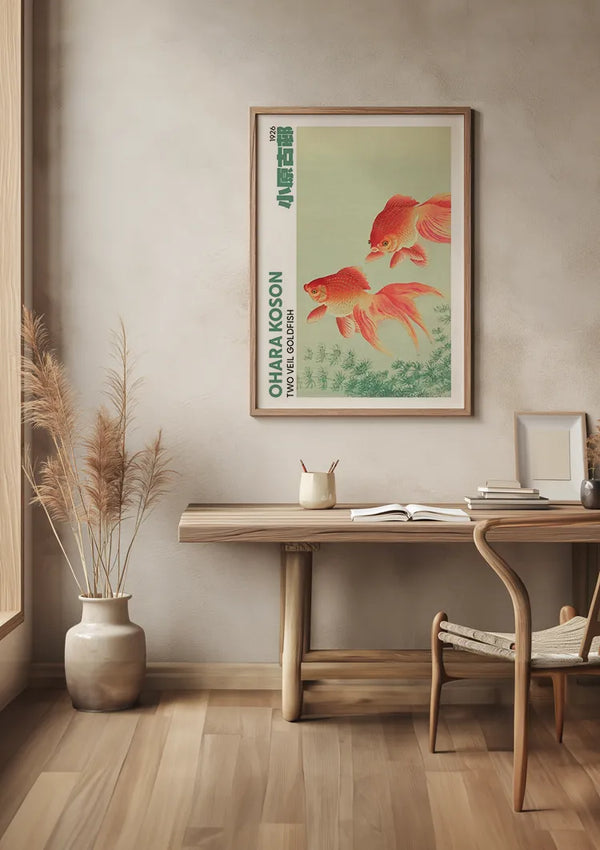 Een minimalistische kamer met een houten bureau, een stoel en een ingelijst O. Koson Two Veil Goldfish Schilderij van CollageDepot aan de muur met een magnetisch ophangsysteem. Naast het bureau staat een vaas met hoge gedroogde planten op de grond. De kamer heeft een strakke, moderne uitstraling met lichte houten vloeren en beige muren.,Lichtbruin