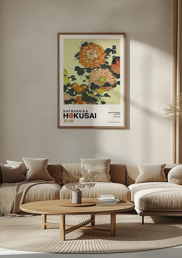 Een woonkamer met een grote ingelijste K. Hokusai Chrysanthenum en Bijenschilderij van CollageDepot aan de muur. Op de voorgrond staat een ronde houten salontafel met decoratieve items, omgeven door een beige sectionele bank versierd met kussens met patronen en een beige deken. De wanddecoratie creëert een elegant middelpunt.,Lichtbruin