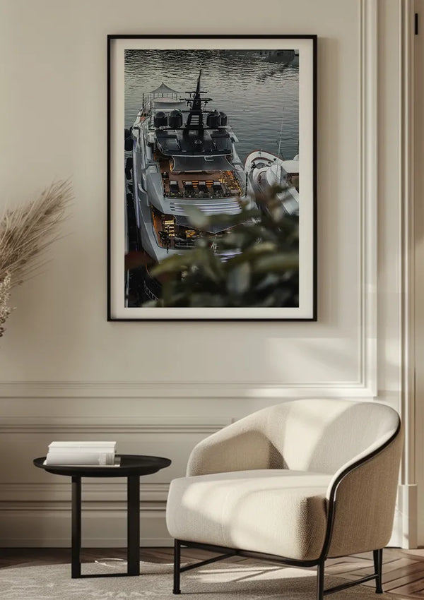 Een Luxe Jacht Schilderij van CollageDepot is met behulp van een magnetisch ophangsysteem gemonteerd op een lichtgekleurde muur boven een moderne stoel met kussens en een kleine ronde tafel met boeken erop in een minimalistische interieursetting.,Zwart