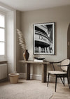 Het minimalistische interieur bestaat uit een houten consoletafel tegen een beige muur, versierd met een vaas met pampasgras. Boven de tafel hangt een ingelijste zwart-witfoto met het CollageDepot Stylish Black And White Dior Logo Schilderij. Een geweven stoel en een rond tapijt met structuur maken de serene sfeer compleet.,Zwart