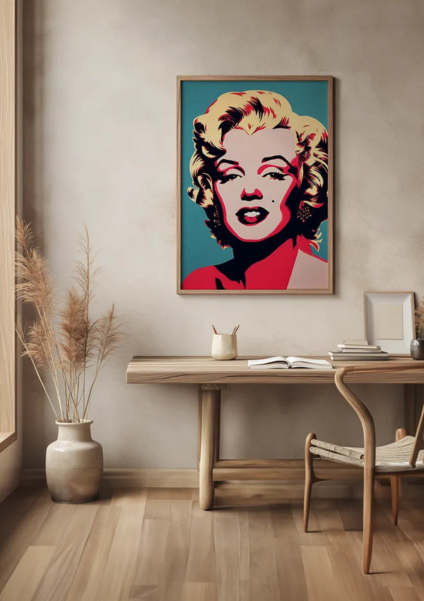 Een minimalistische kamer met een houten bureau en stoel, met een grote, ingelijste Marilyn Monroe In Popart Schilderij van CollageDepot aan de muur. Op het bureau staan een notitieboekje, een pen en een kleine stapel boeken. Links van het bureau staat een vaas met gedroogde planten op de vloer, wat de wanddecoratie versterkt.