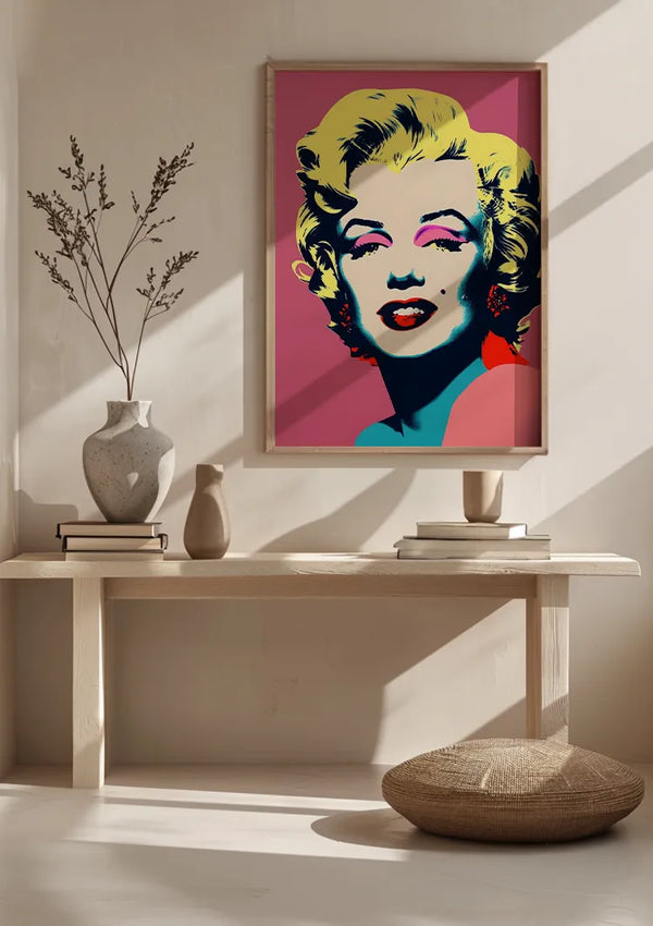 Een minimalistisch interieur met een houten bank tegen een muur. Op de bank staan een paar vazen en een boek. Boven de bank is een CollageDepot Iconische Marilyn Monroe Popart Schilderij ingelijst als wanddecoratie aan de muur. Op de grond ligt een rond geweven kussen.