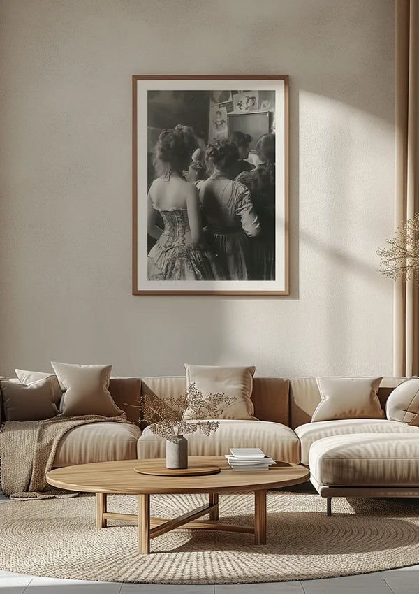 Een moderne woonkamer heeft een grote, ingelijste zwart-witfoto aan de muur, beveiligd met een Vintage Dames In Een Rij Schilderij van CollageDepot. De kamer is voorzien van een lichtbruine bank met lichtbeige en witte kussens, een ronde houten salontafel met decoratieve items en een lichtgekleurd, minimalistisch decor.,Lichtbruin